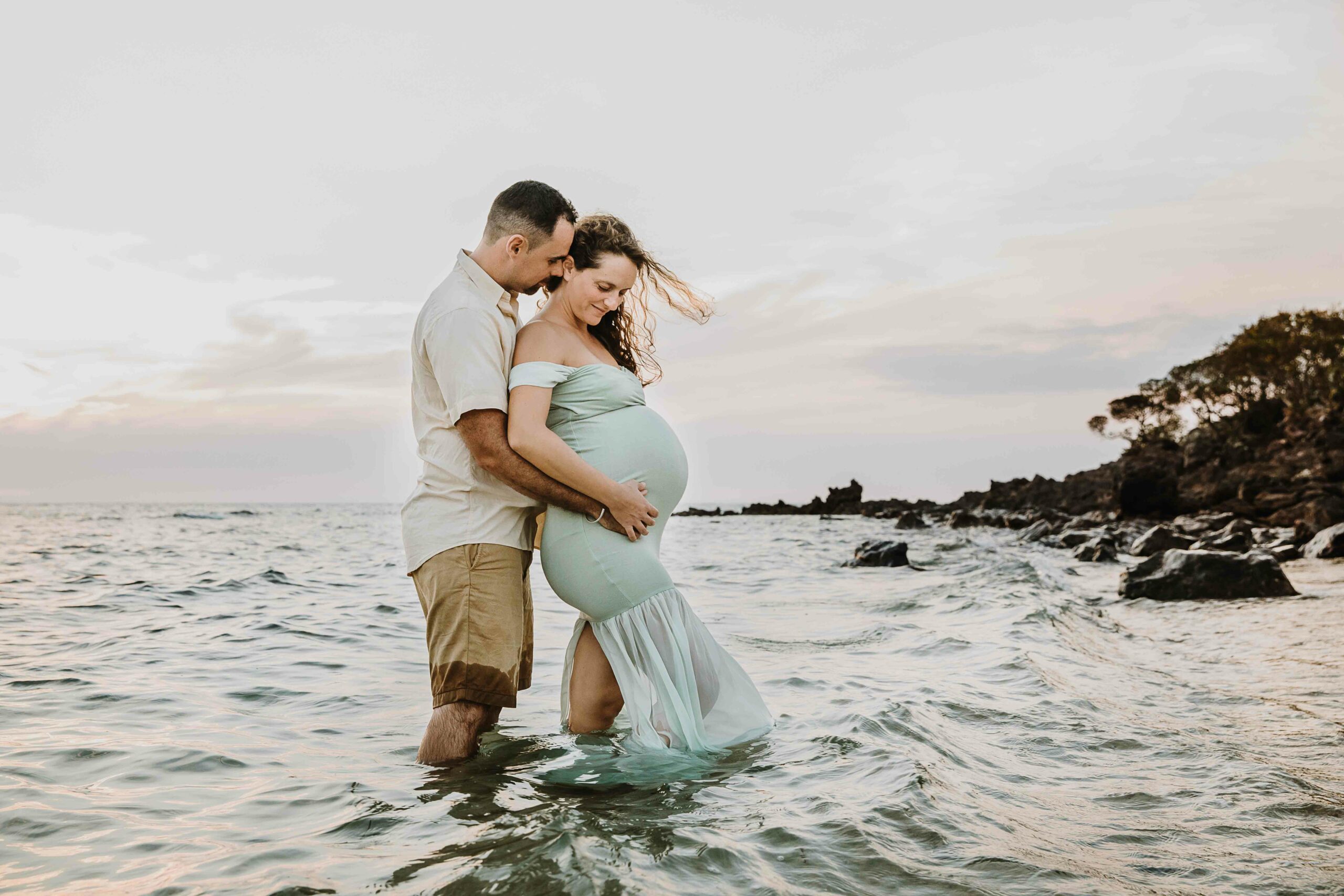 un homme et sa femme enceinte enlacés, les pieds dans la mer