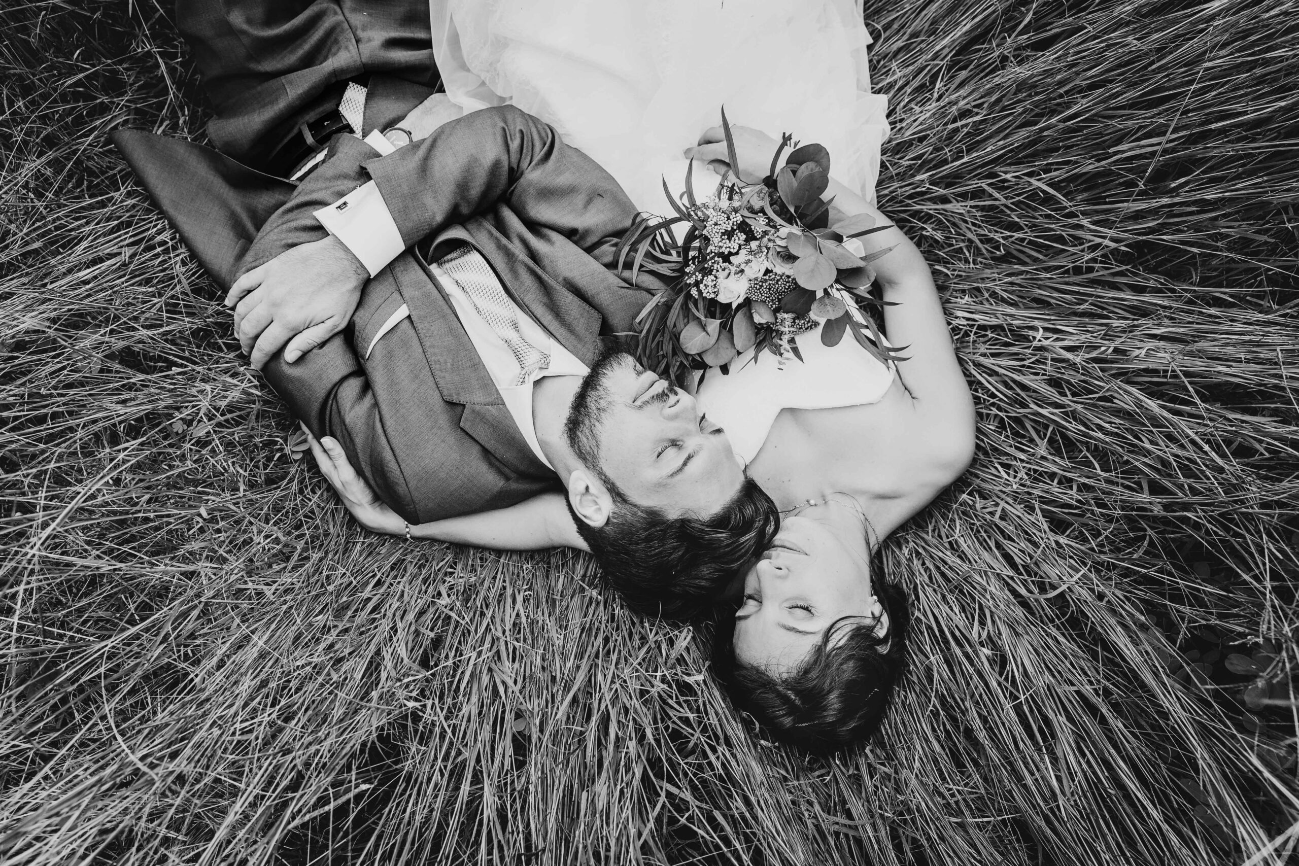 photo noir et blanc, les mariés sont allongés dans l'herbe les yeux fermés