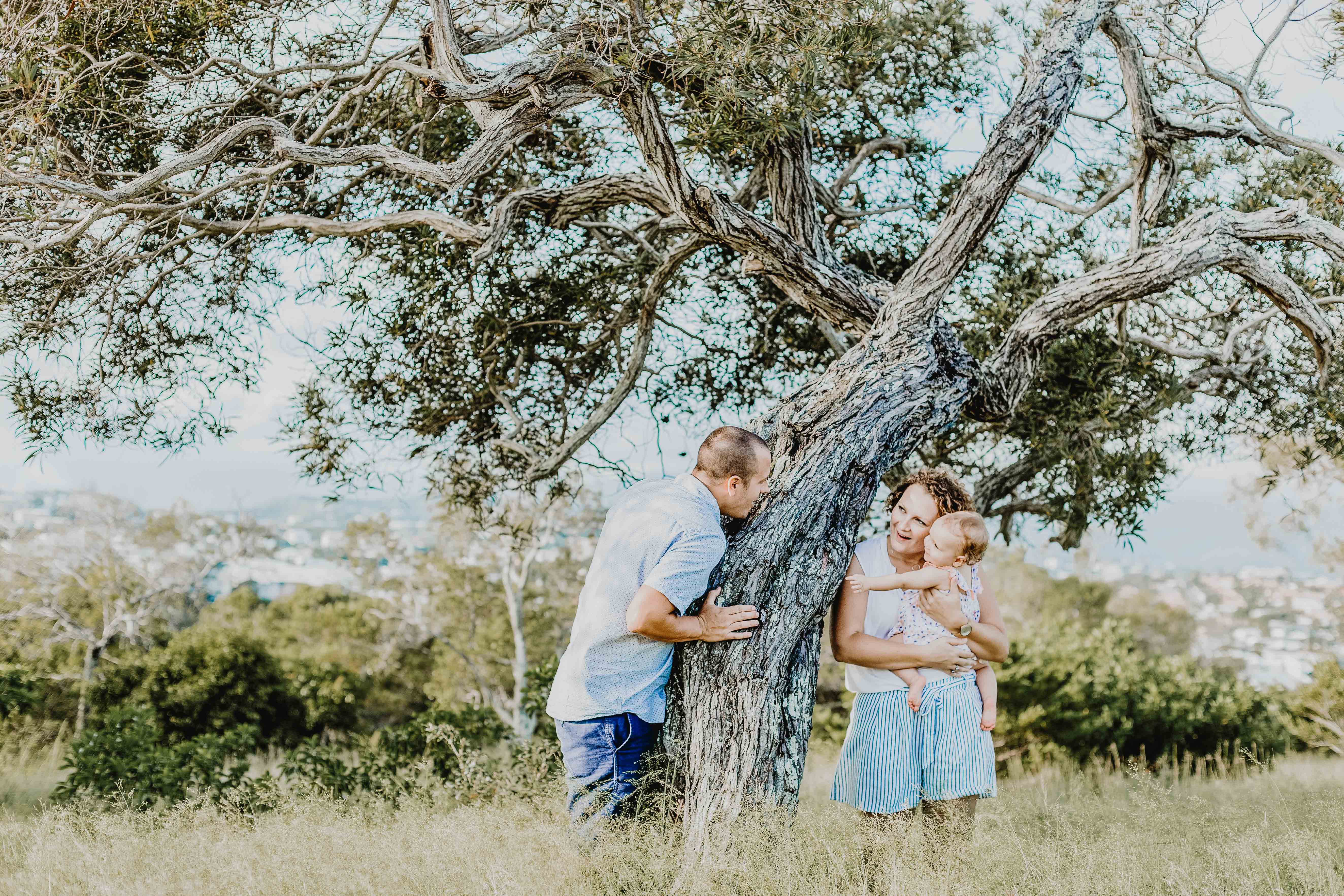 séance photo famille lifestyle en extérieur. les parents portent bébé près d'un arbre