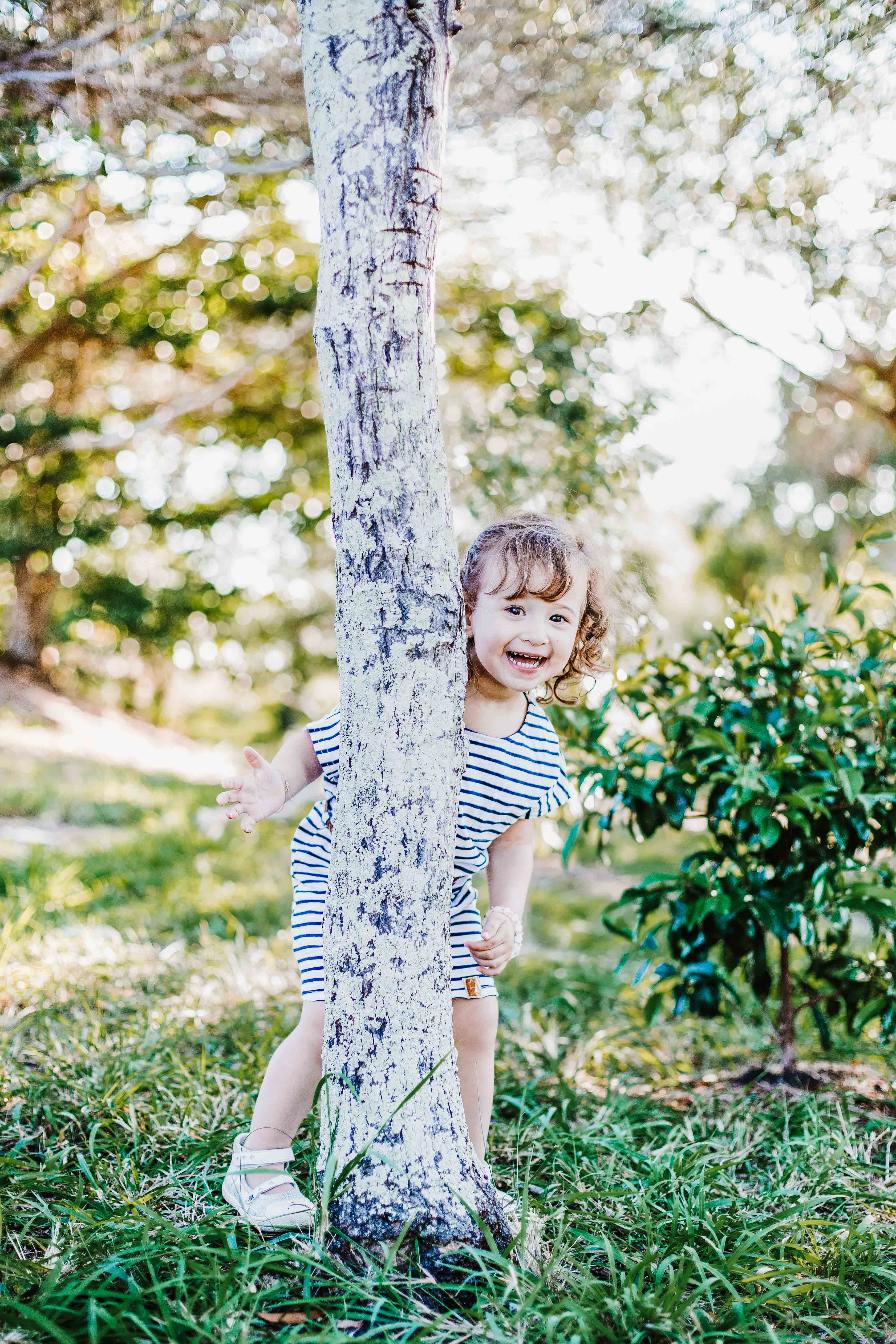une pettine fille se cache derrière un arbre dans la foret séance photo lifestyle