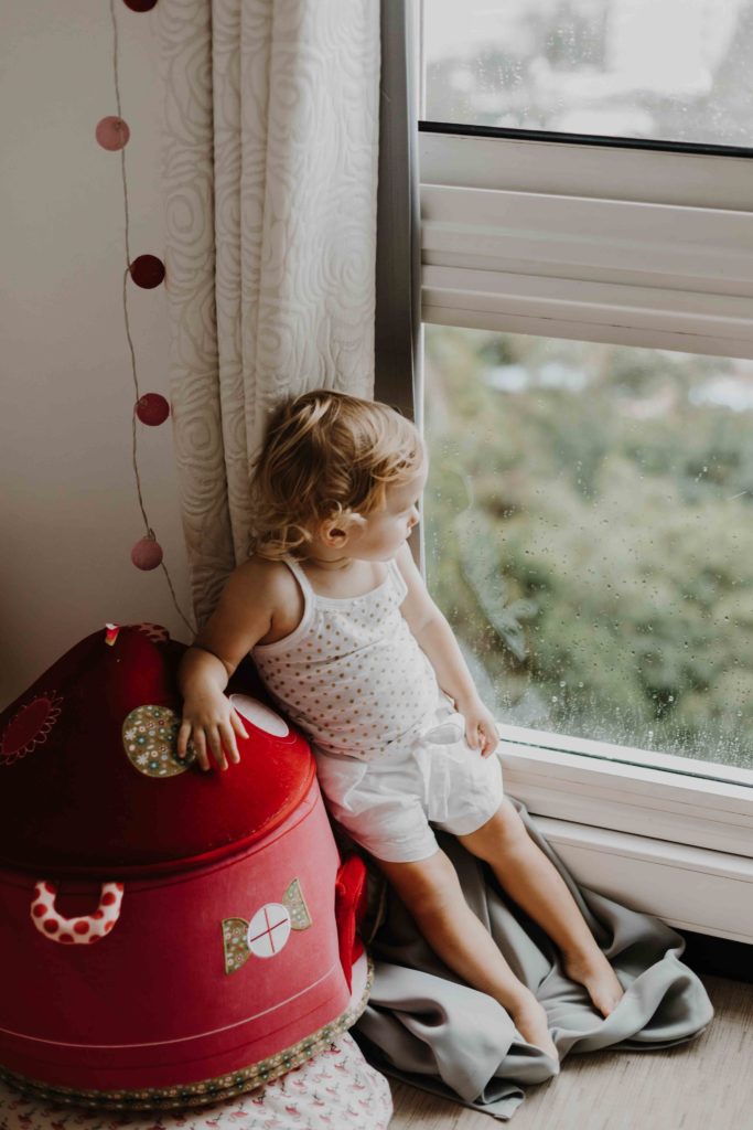 photographe famille lifestyle à domicile, immortaliser des moments de complicité et de douceur dans votre environnement quotidien. L'enfant regarde par la fenêtre de sa chambre à Brunstatt.
