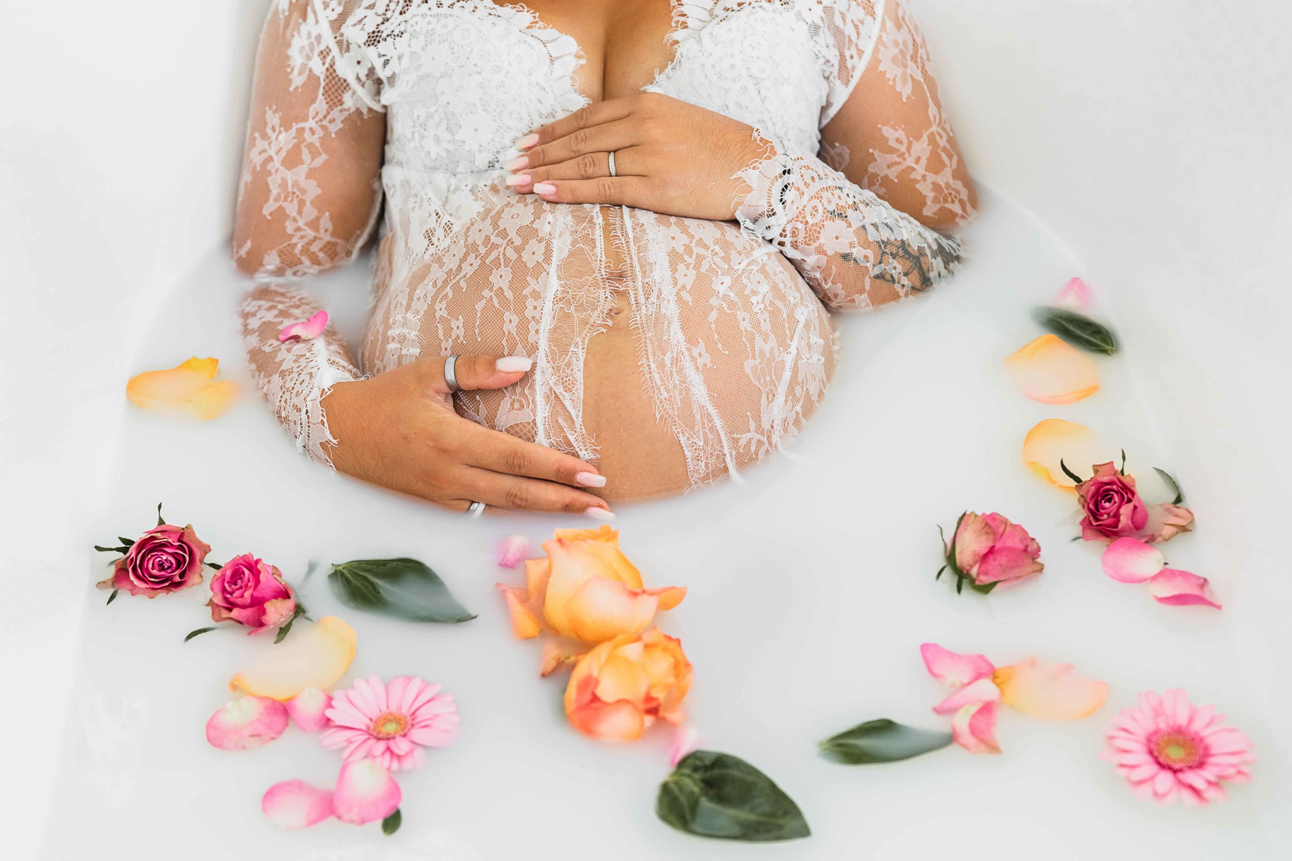 femme enceinte dans une robe en dentelle blanche, dans un bain de lait avec des fleurs . Gros plan sur le ventre de la maman