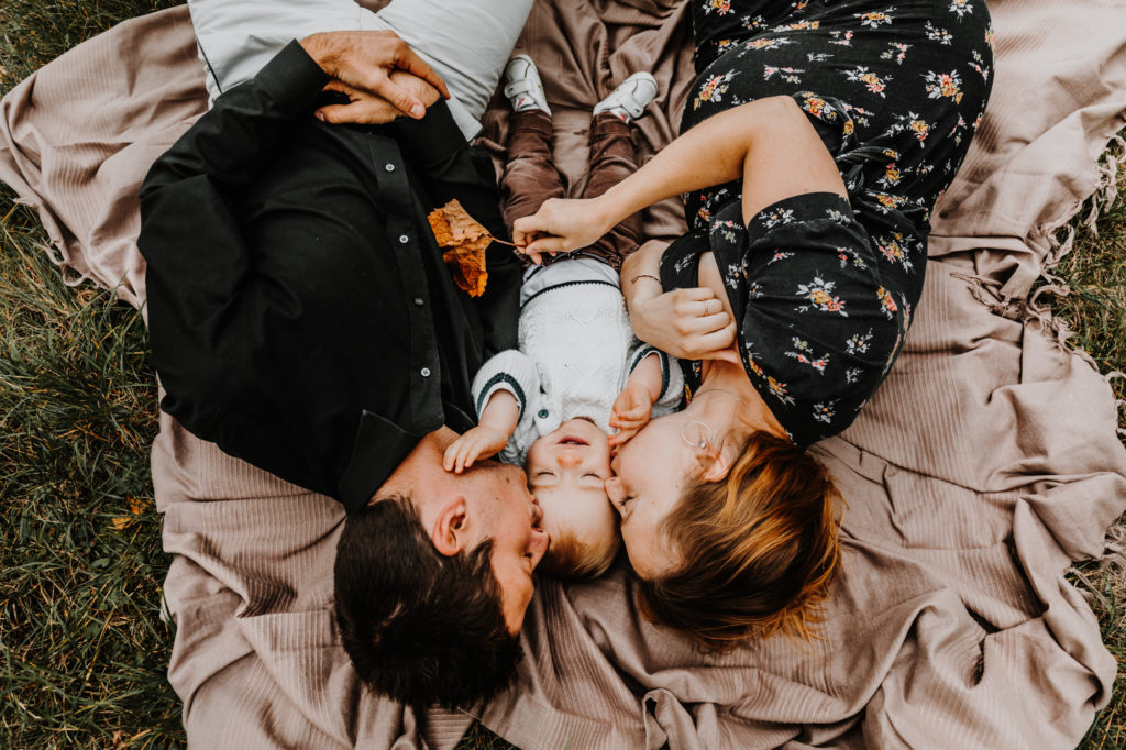 une famille allongée sur une couverture dans les vignes joue avec le bébé