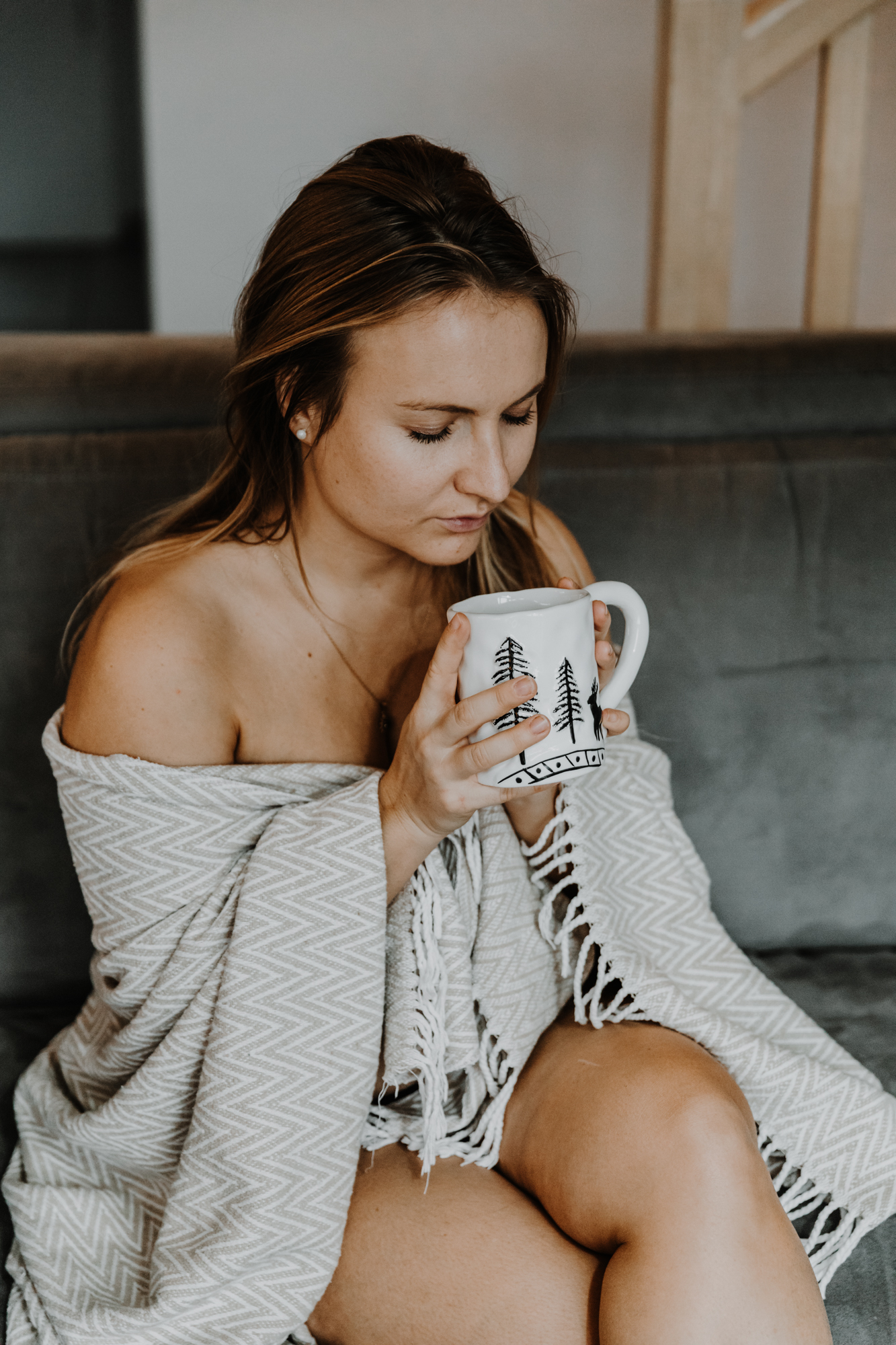 jeune femme assise sur un canapé, nue sous sa couverture, tient une tasse de thé