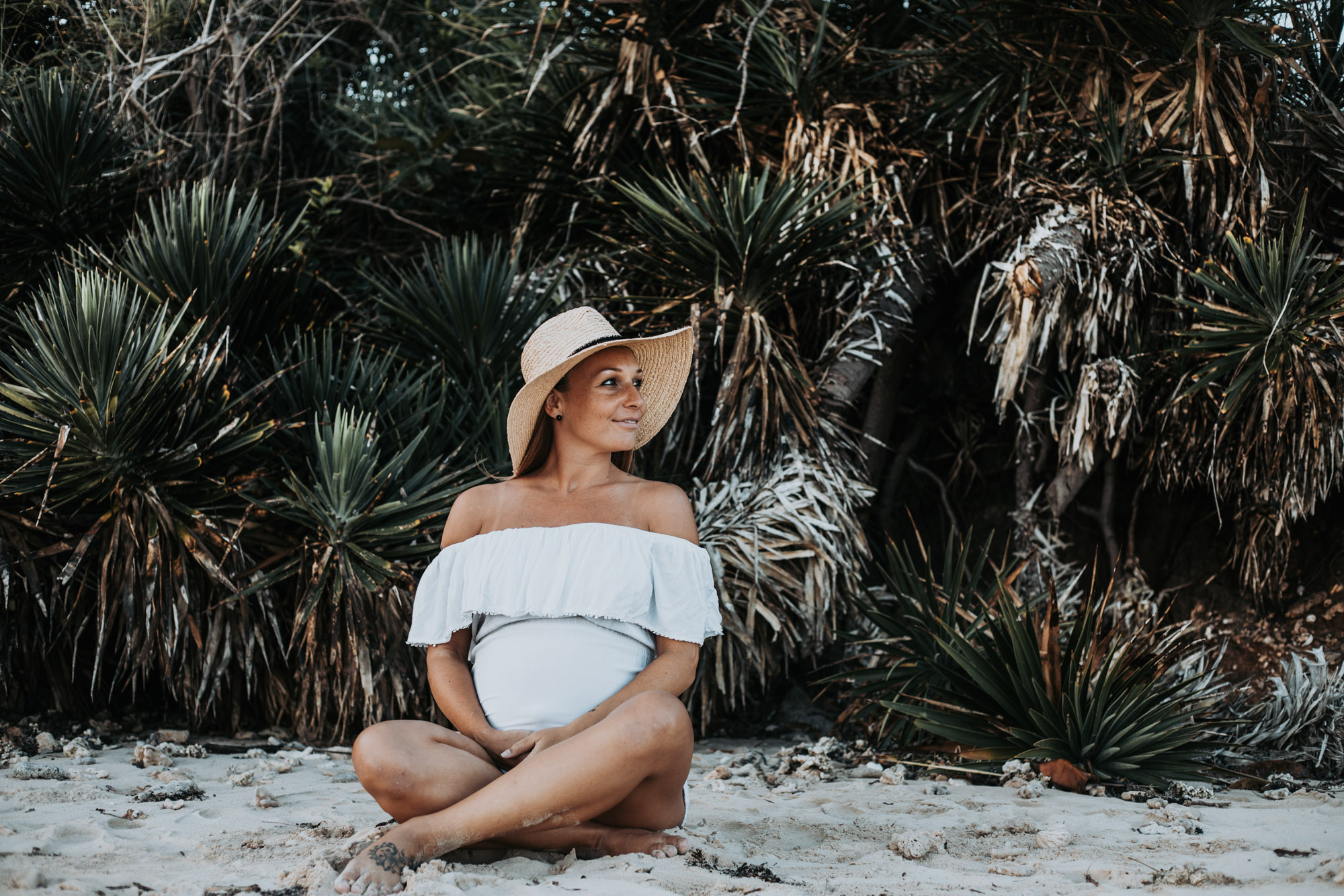 femme enceinte portant un chapeau, assise dans le sable