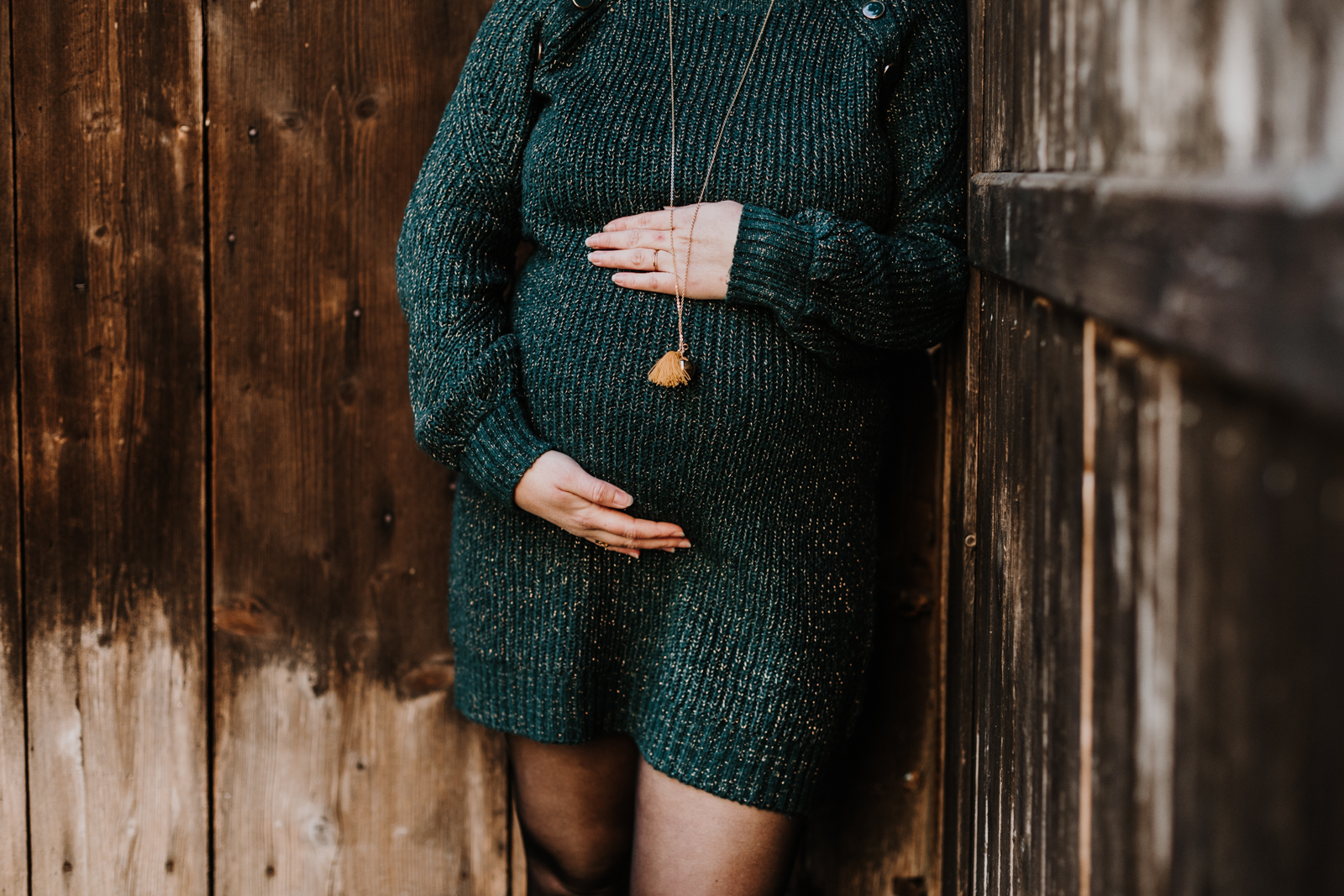 détail du ventre de femme enceinte adossée contre une vieille porte de grange en bois