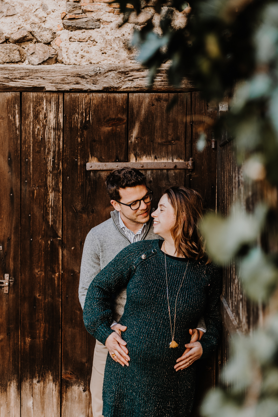 couple adossé à un vieux mur en bois, le feuillage les cache à moitié