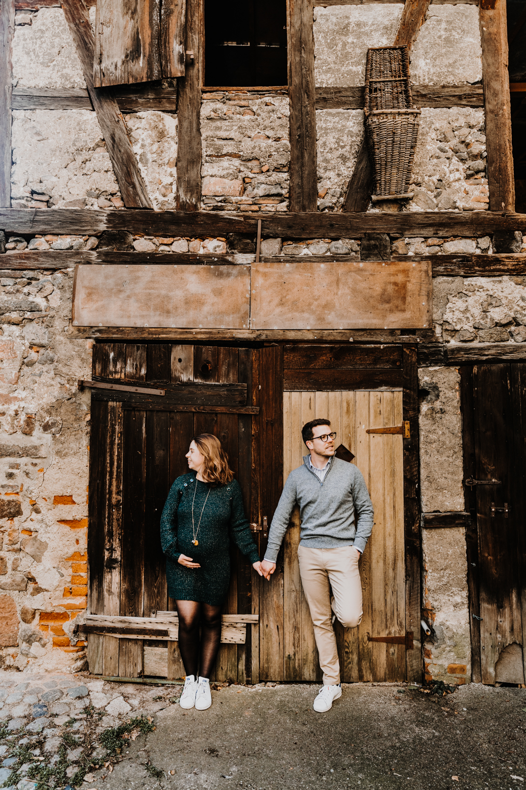 une femme enceinte et un homme se tiennent la main, adossés à une vieille porte en bois de grande dans le village de Kaysersberg en alsace