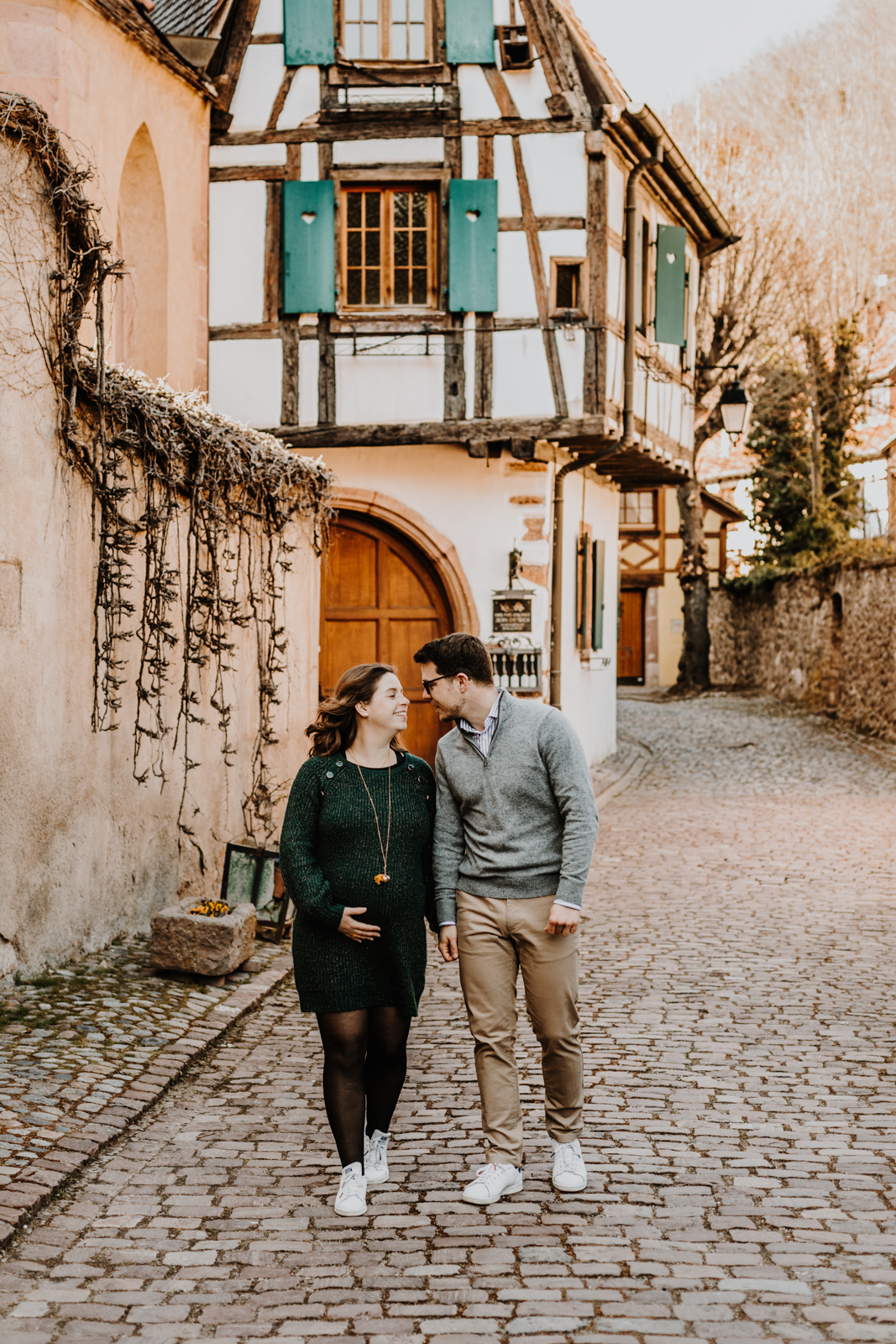 un couple, une femme enceinte et un homme marchent en s'embrassant dans une rue du village de Kaysersberg en alsace