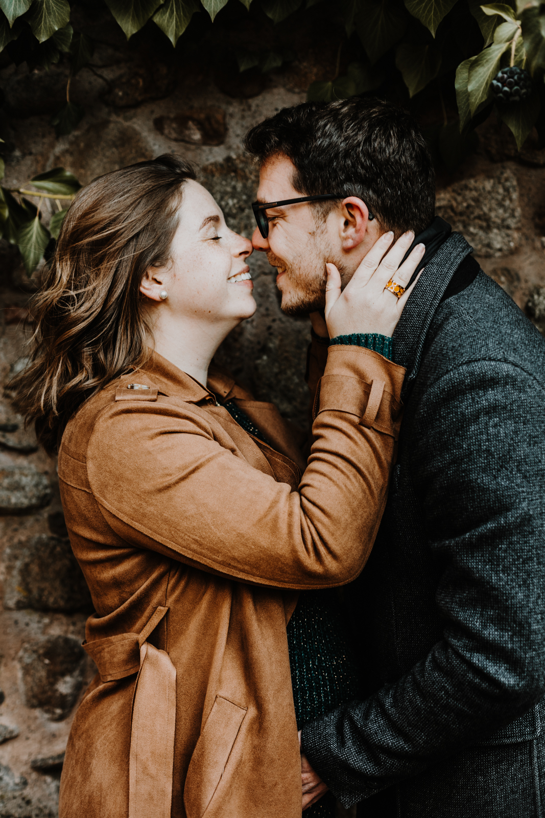 un homme et une femme s'embrassent devant un mur en pierres recouvert de végétation