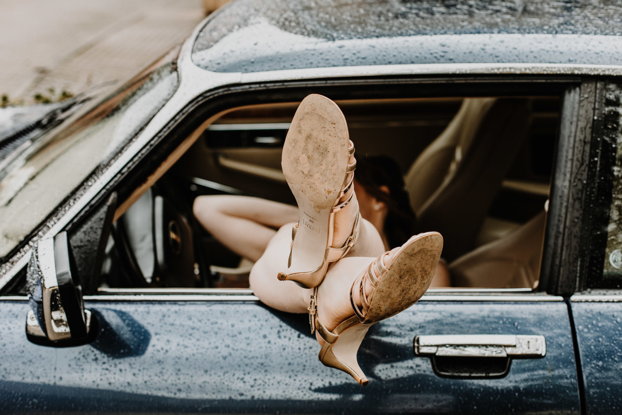 la mariée allongée dans la voiture ancienne, ses jambes dépassent de la fenêtre