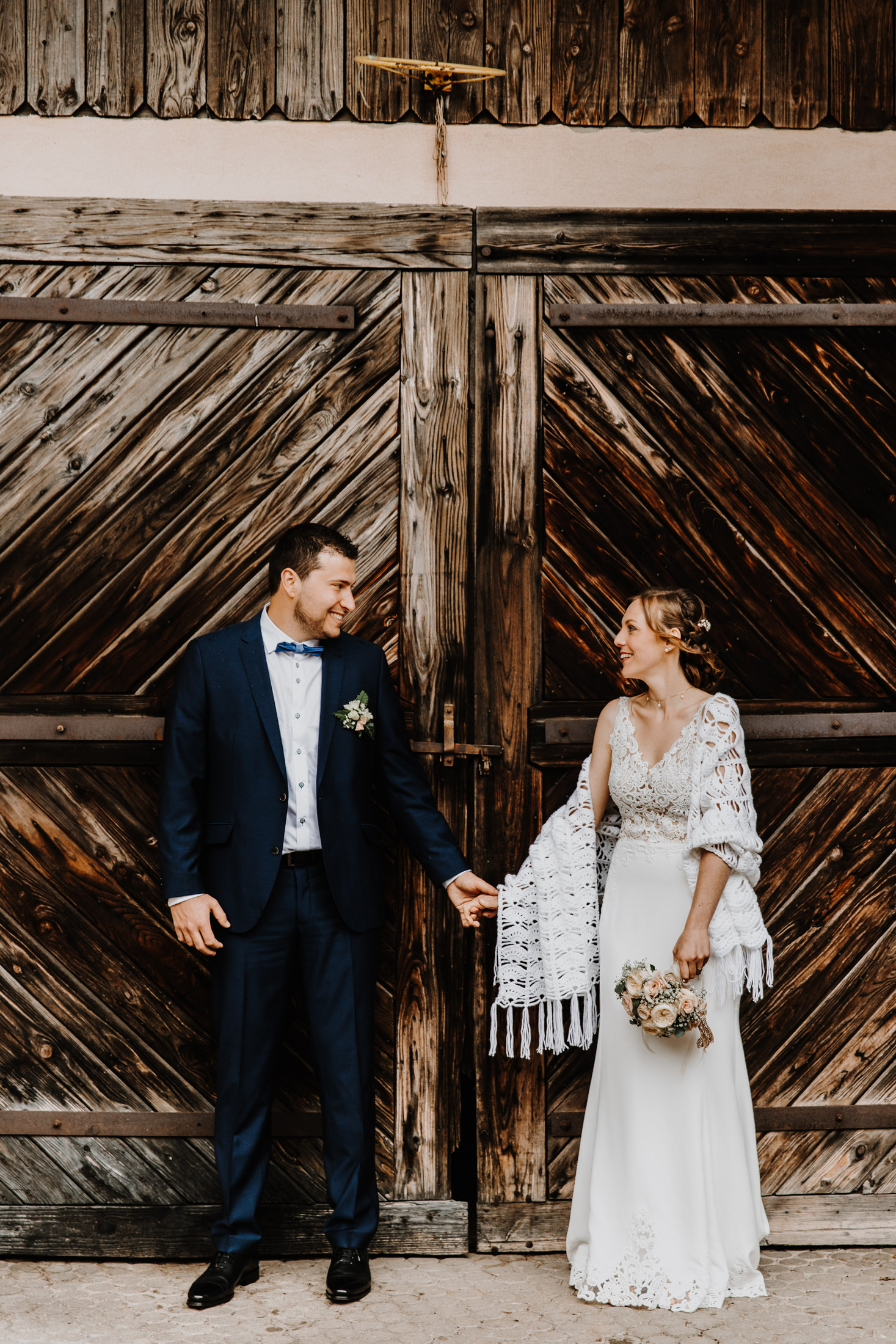 les mariés côte à côte, se tiennent la main devant une vieille porte en bois