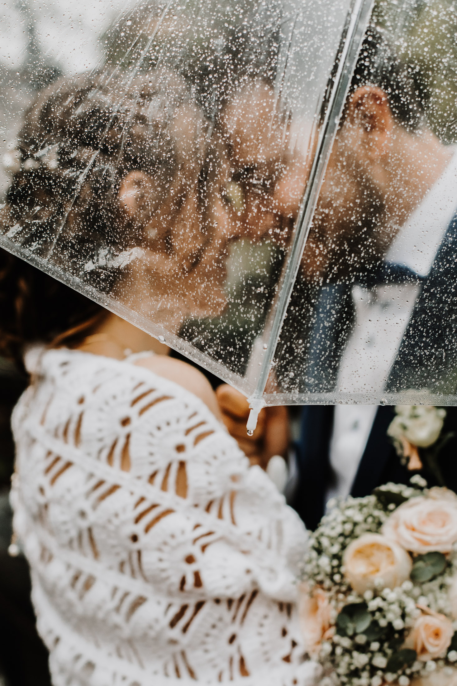 les mariés face à face, enlacés sous un parapluie trnasparent