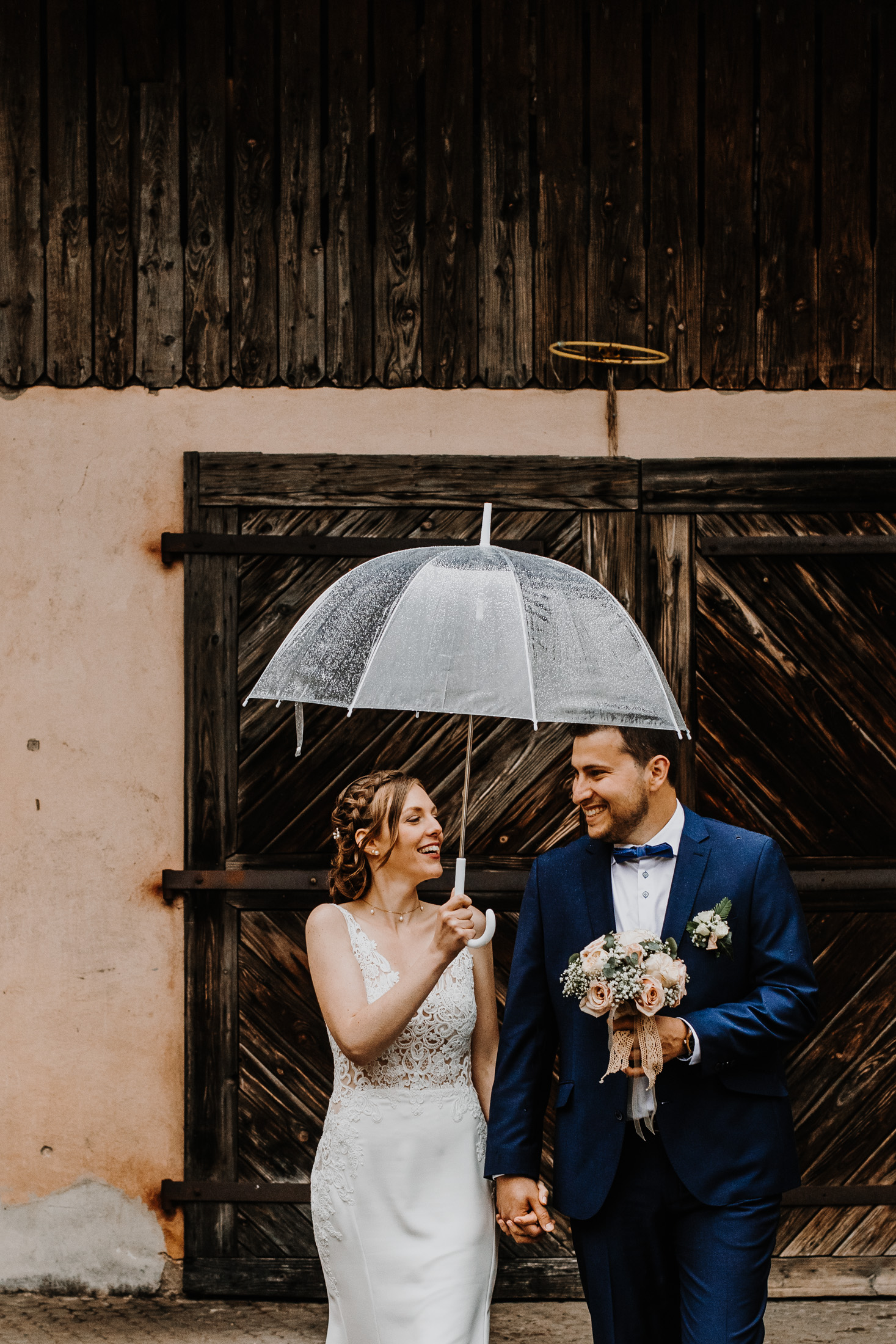 les mariés marchent sous la pluie, dans une ancienne cour, sous un parapluie transparent