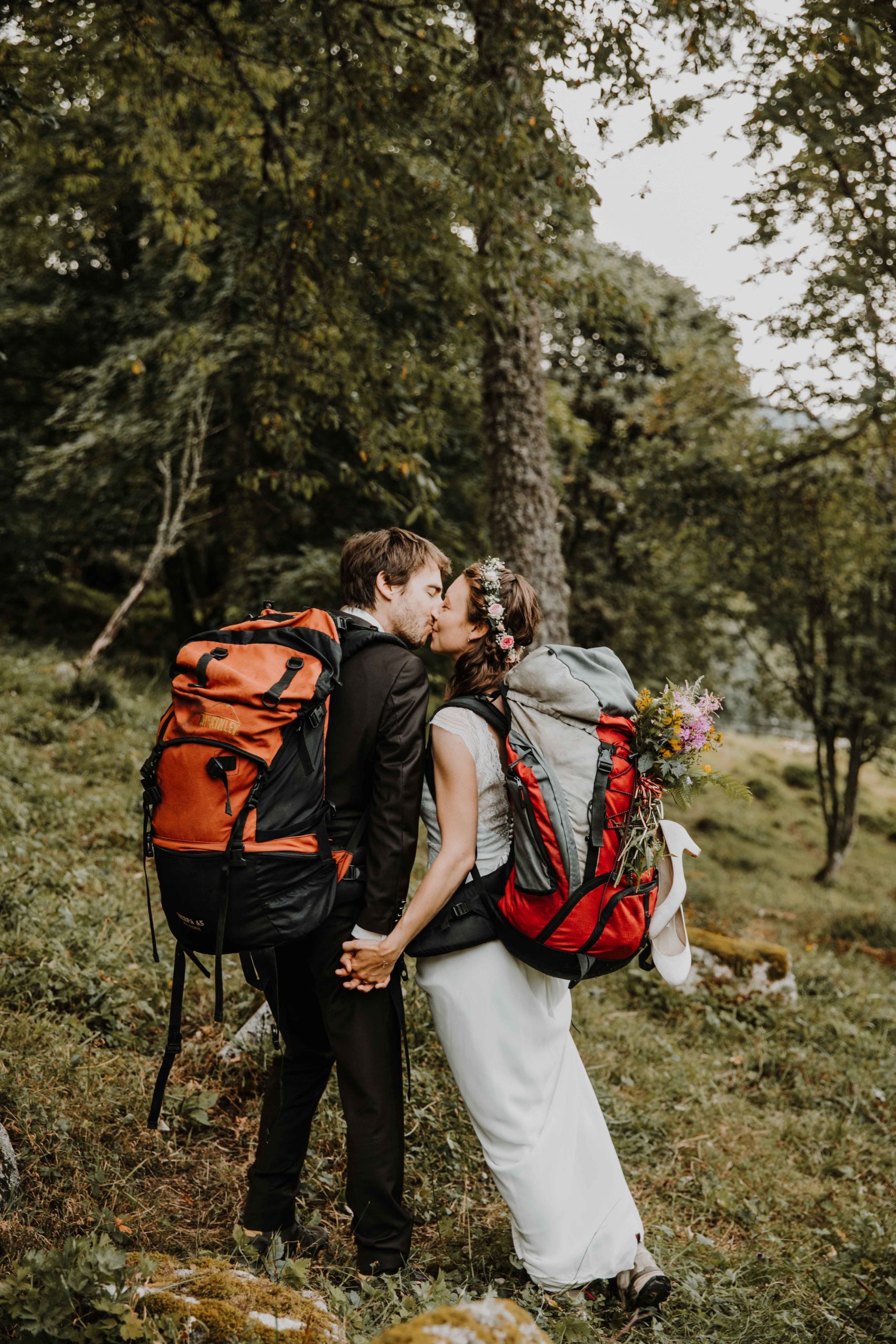 les mariés portent un sac à dos de randonnée et s'embrassent dans la forêt
