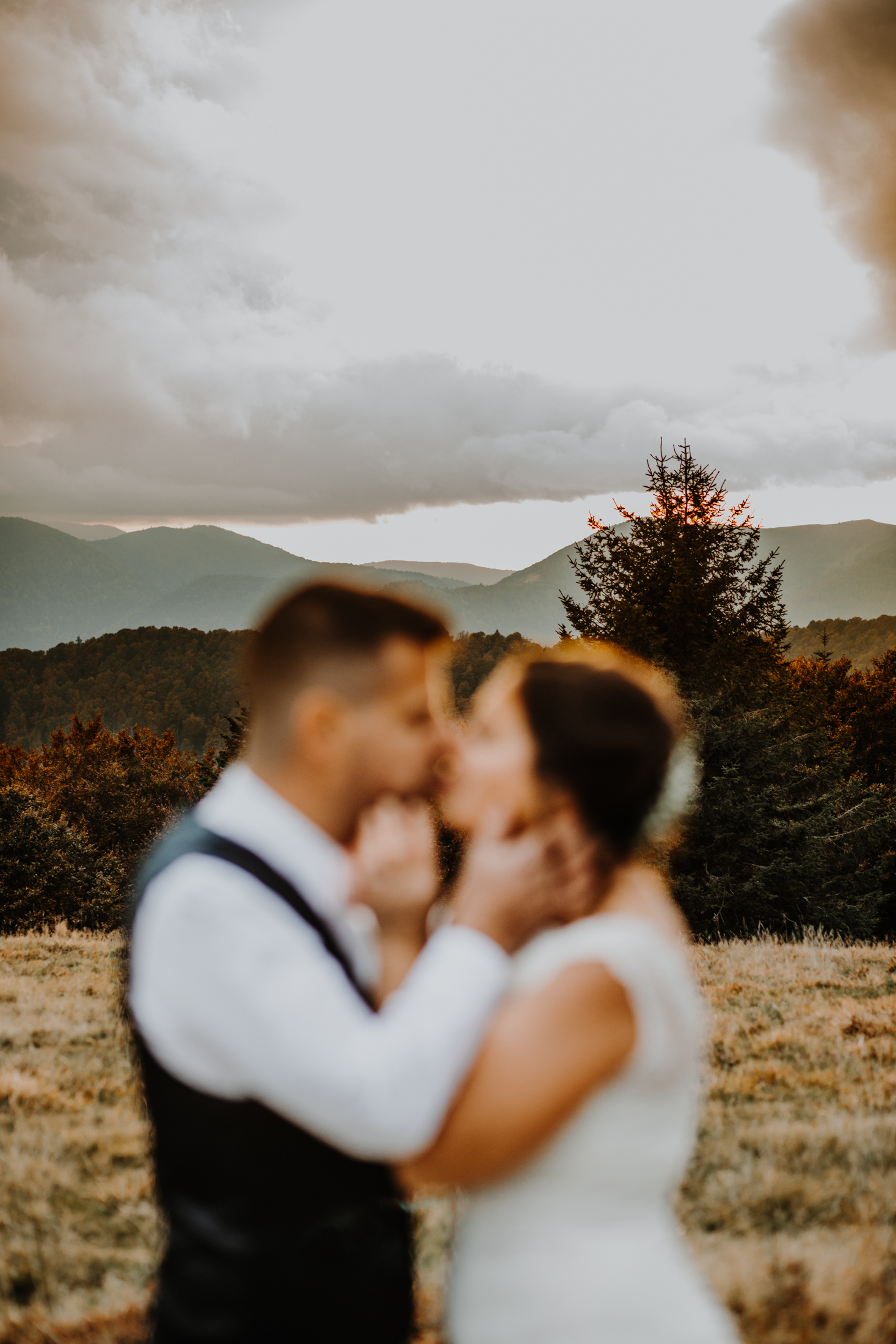 couple de mariés enlacés, tête à tête dans un décor de montagne au coucher du soleil