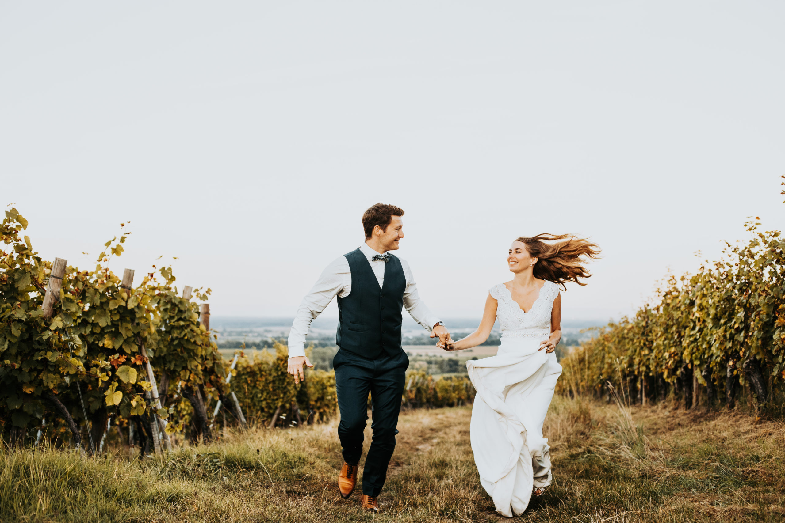 couple de mariés courent en riant, main dans la main dans les vignes