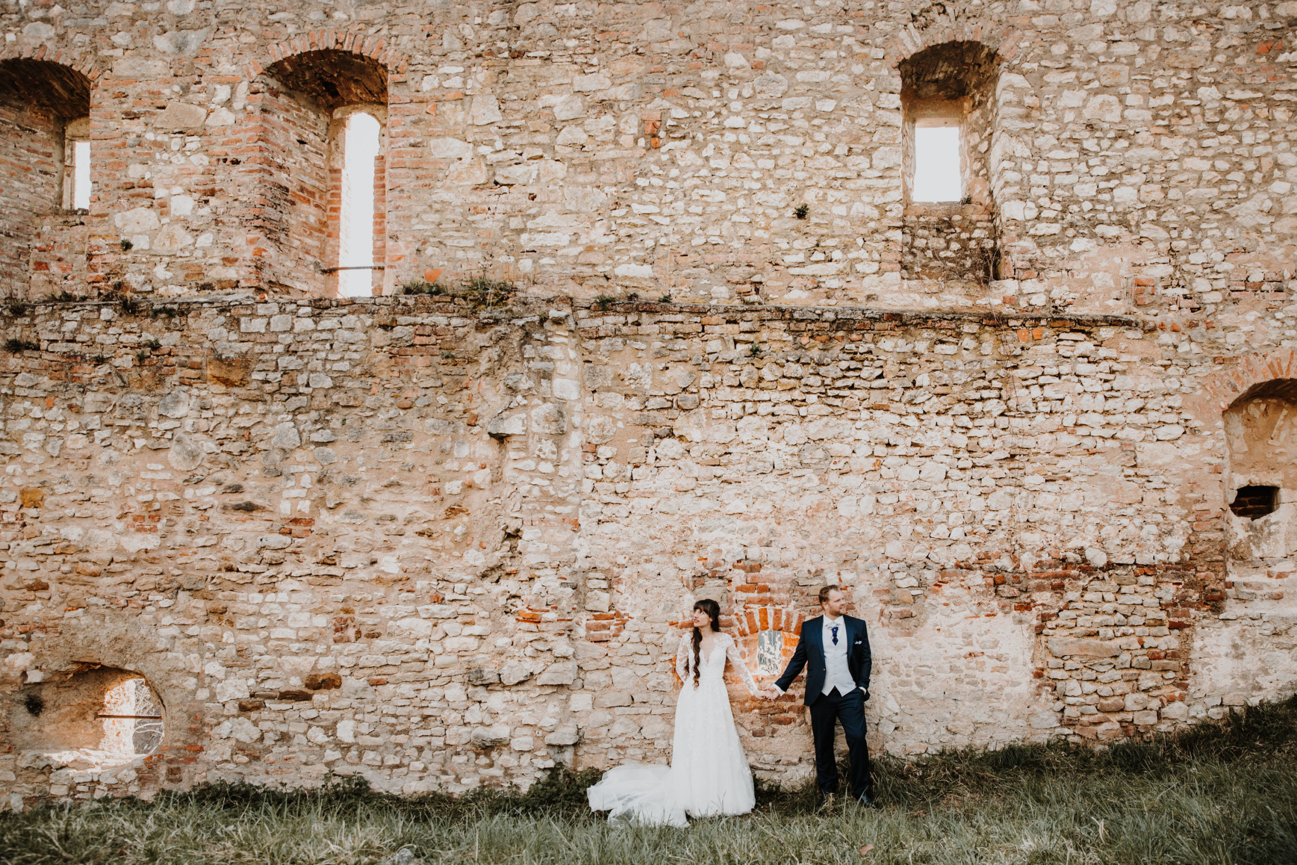 les mariés se tiennent la mai adossés à un vieux mur en pierre d'un château en ruine