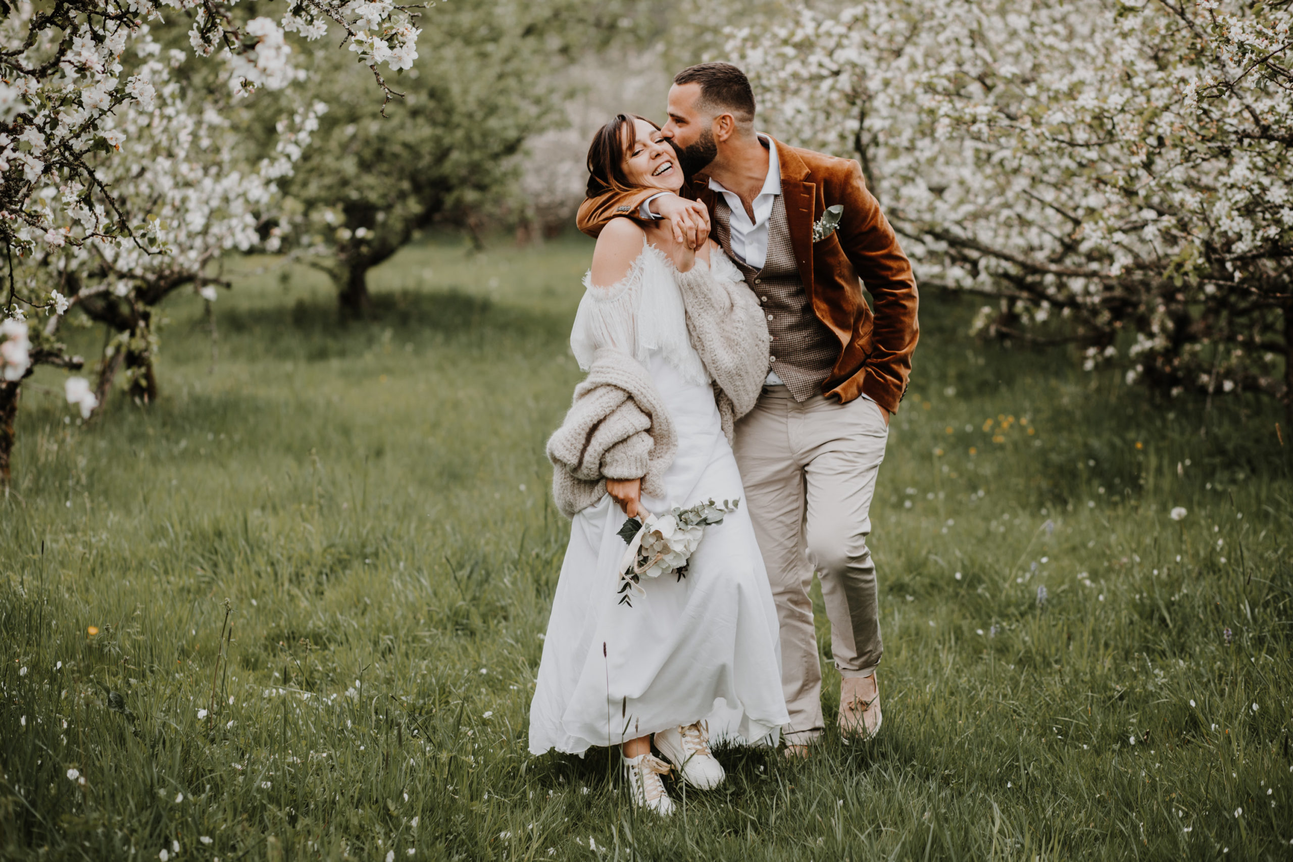 les mariés marchent en riant dans un verger en fleurs domaine saint loup
