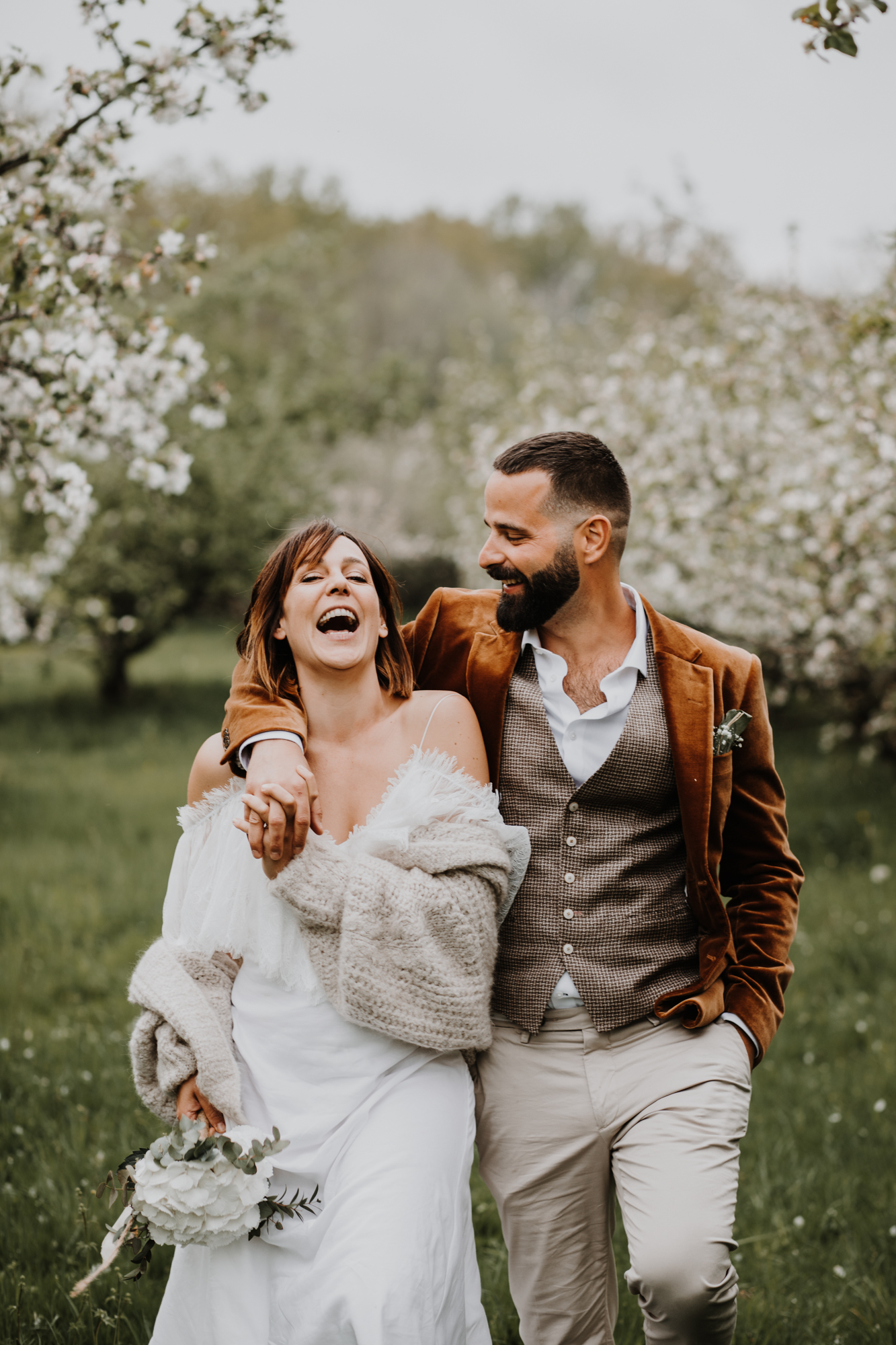 les mariés marchent en riant dans un verger en fleurs domaine saint loup