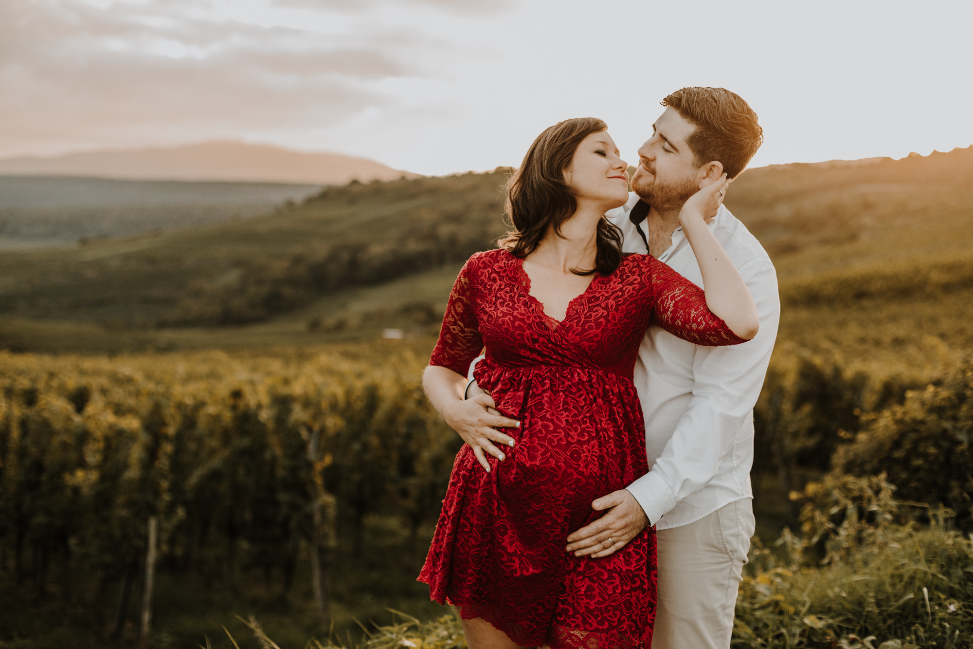 une femme enceinte et son mari enlacés dans les vignes au coucher du soleil