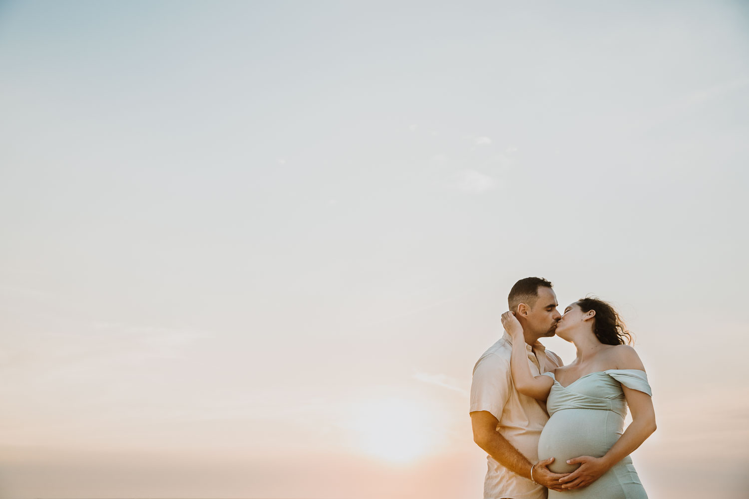 une femme enceinte embrasse son mari au coucher du soleil