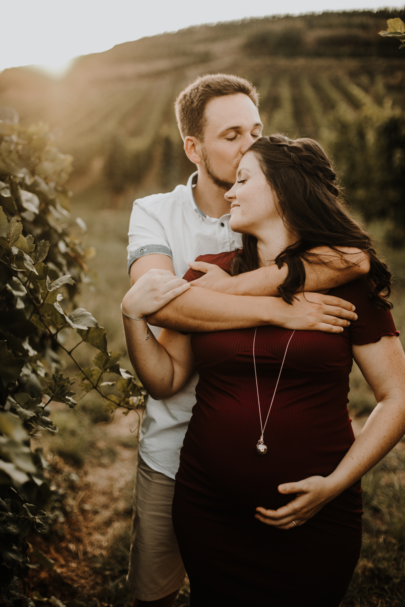 une femme enceinte dans les bras de son mari dans les vignes au coucher du soleil