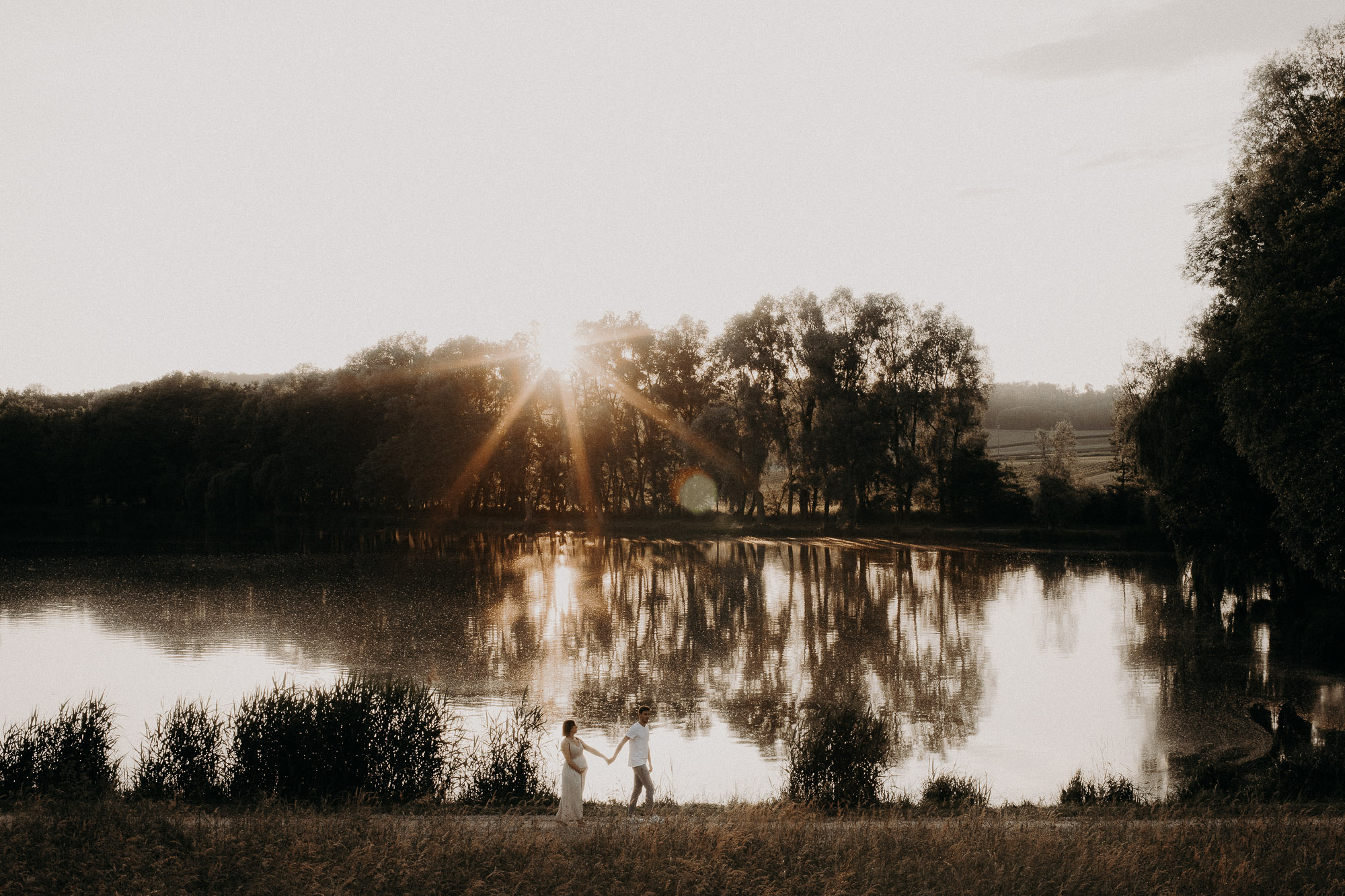 couple et femme enceinte marchent dans un paysage de coucher de soleil devant un lac